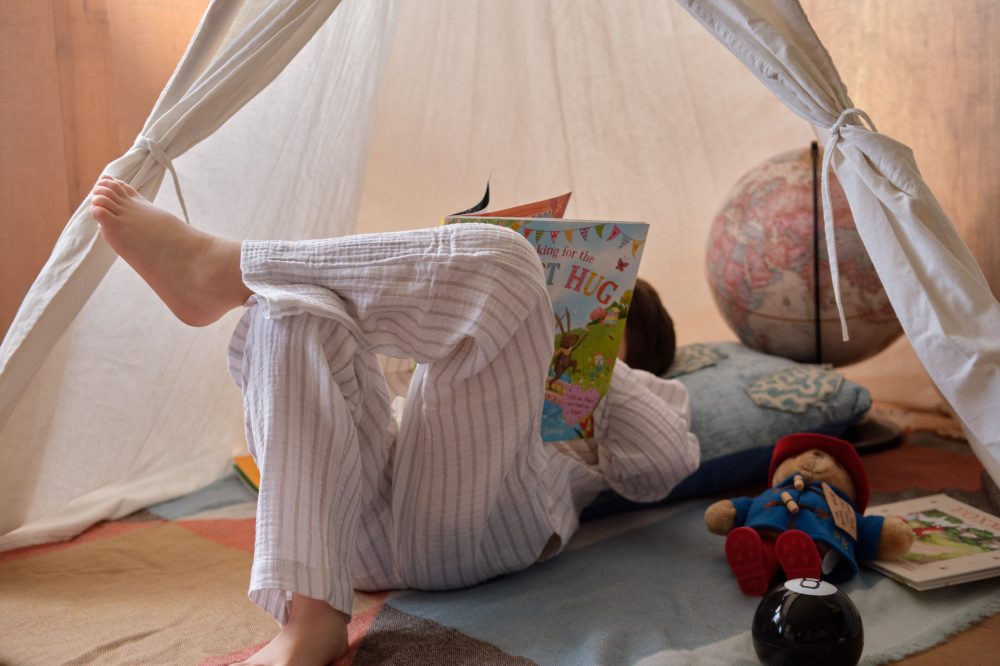 A child lying down in a teepee reading a book