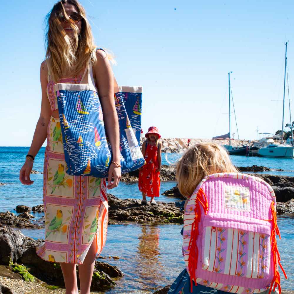 A woman and children on a beach with colourful bags from the Maison Mangostan x Studio Noos collaboration 