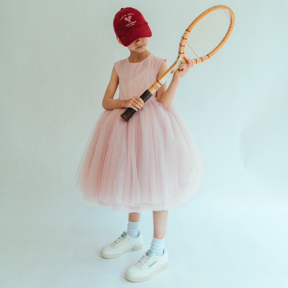 A girl in a pink occasionwear dress and cap holding a racket 