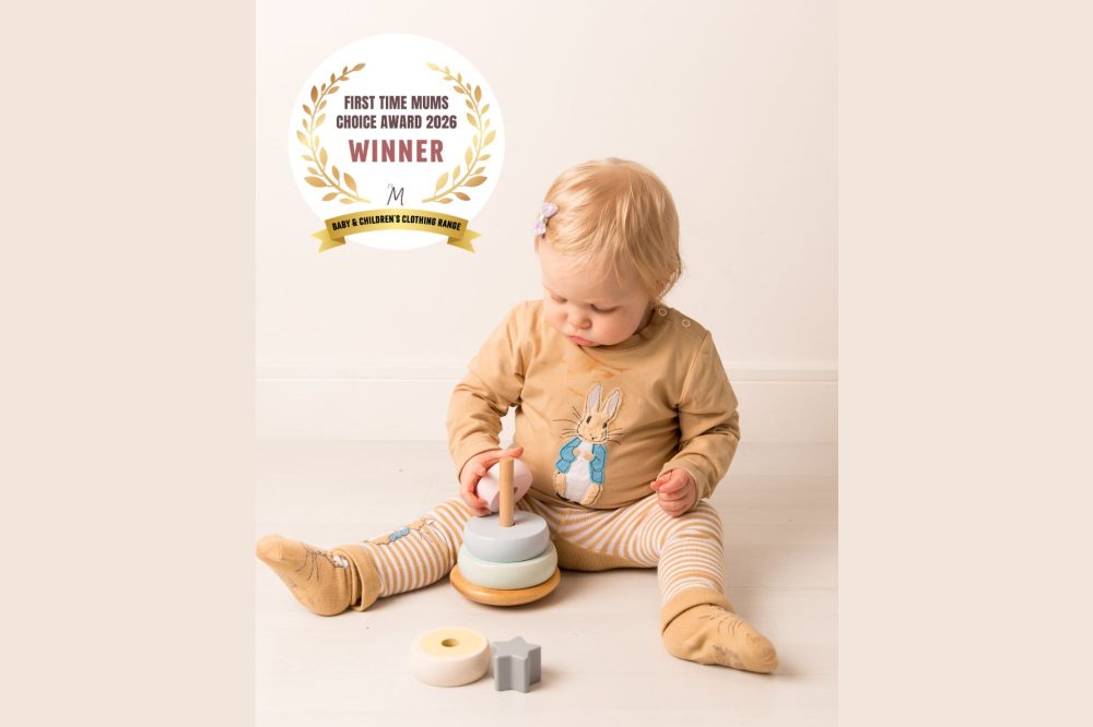 A baby sat on the floor playing with a stacker toy and wearing a top and leggings from the Blade & Rose Peter Rabbit Neutral Collection