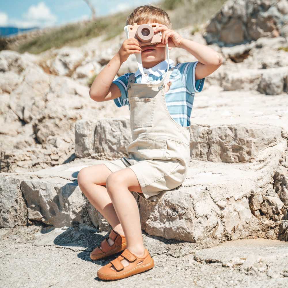 A boy sat on some rocks holding a toy camera to his eye