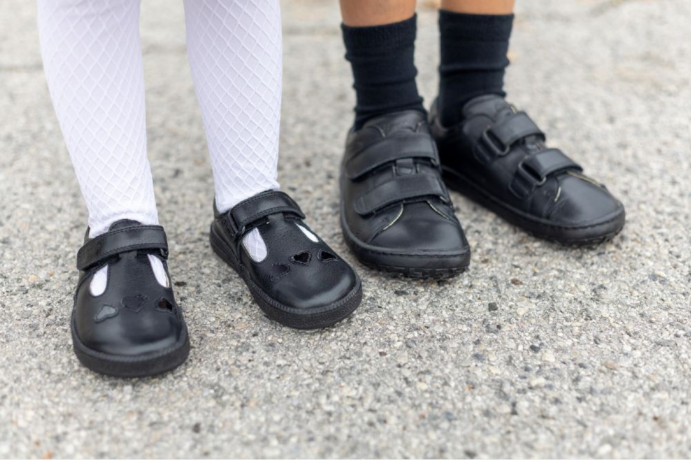 Two pairs of children's feet wearing black school shoes by Froddo