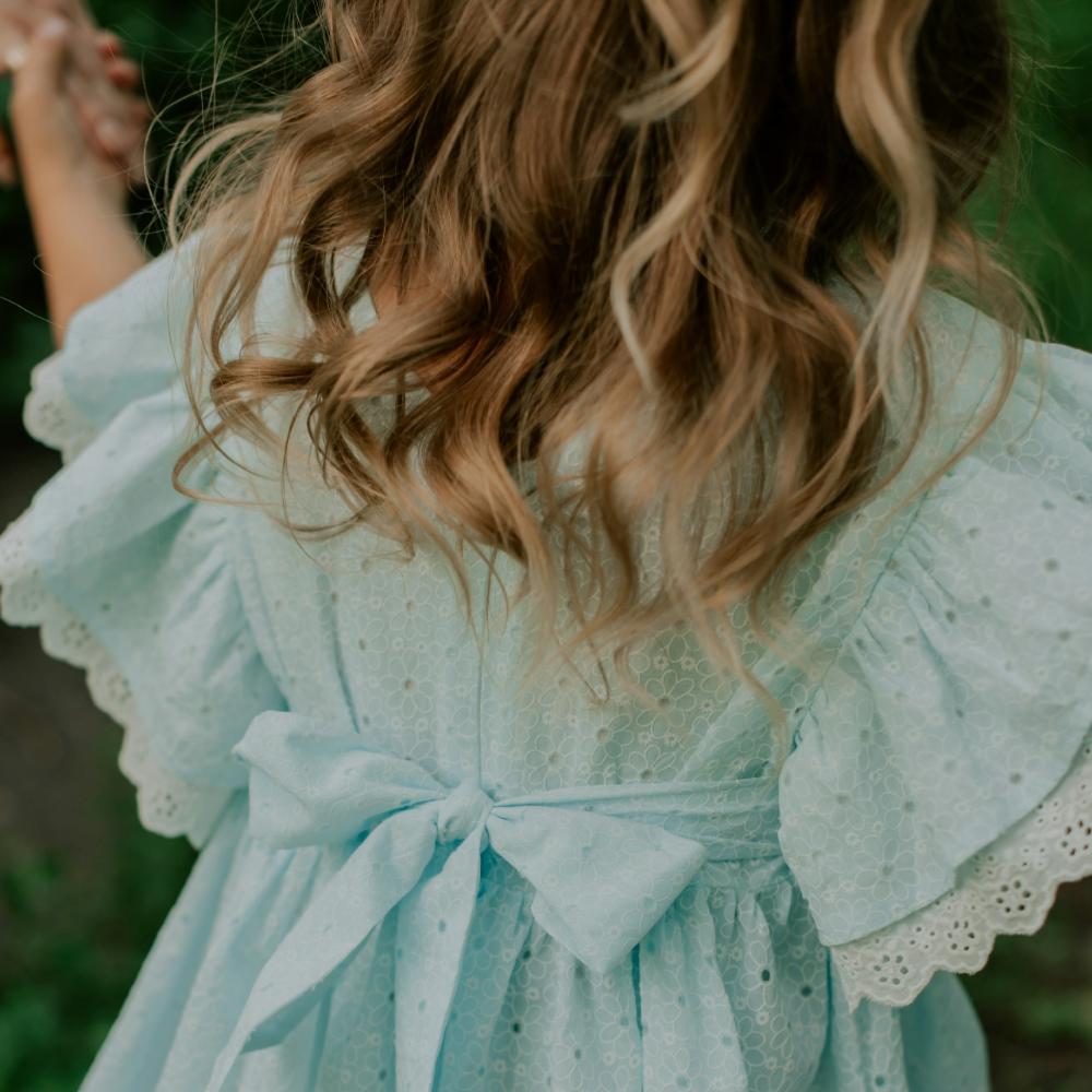 The back of a child wearing a pale blue summer dress with a bow 