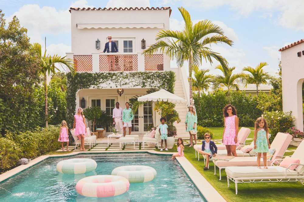 A family stood at the back of a villa with a pool wearing coordinating outfits from the Lilly Pulitzer x Janie and Jack collaboration 