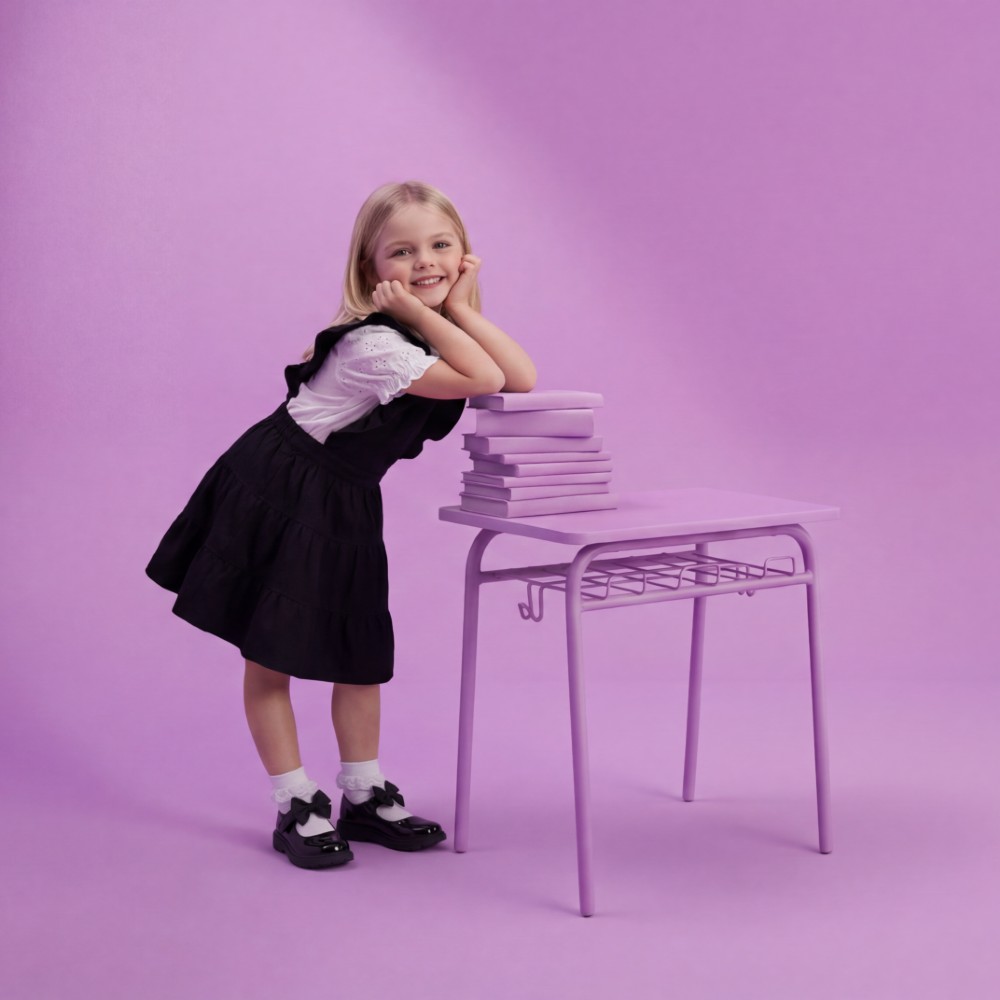 A girl leaning on a lilac desk wearing a black school dress and white top by Lelli Kelly Schoolwear
