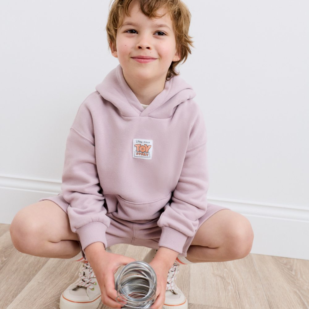 A boy crouched down holding a slinky toy wearing a lilac hoody and matching shorts from the M&S Kids Toy Story collection