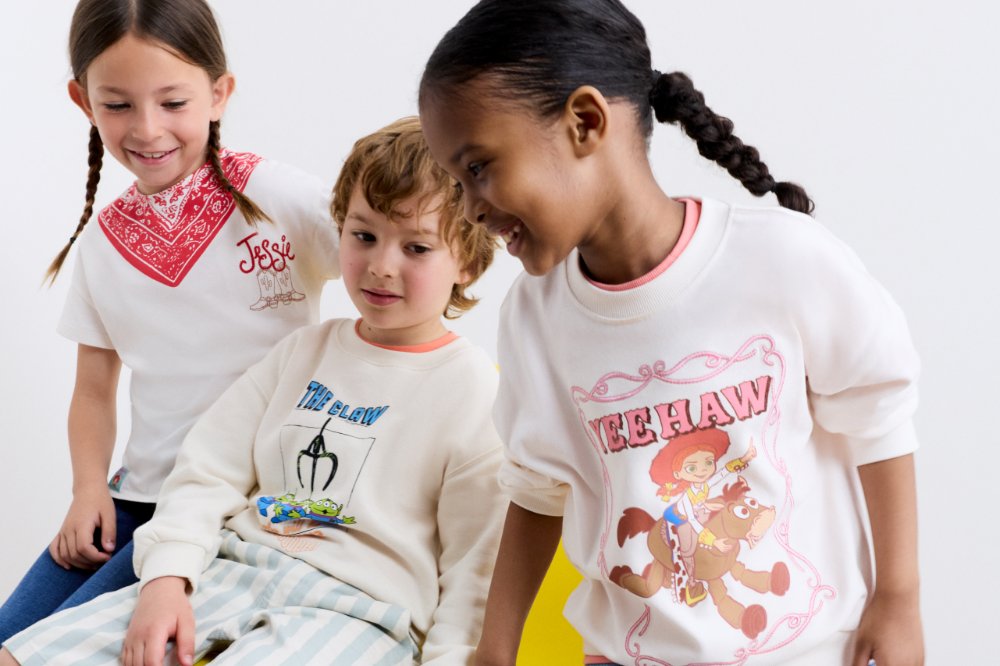 Three children resting on a bright yellow chair wearing outfits from the M&S Kids Toy Story collection