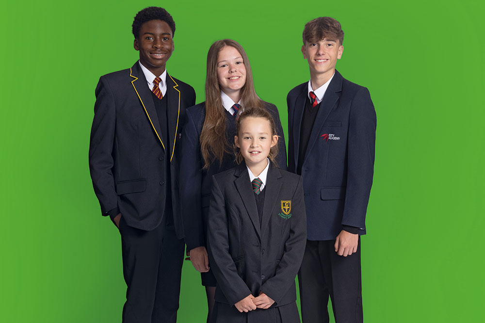 Four children stood against a green background wearing One+All school uniform