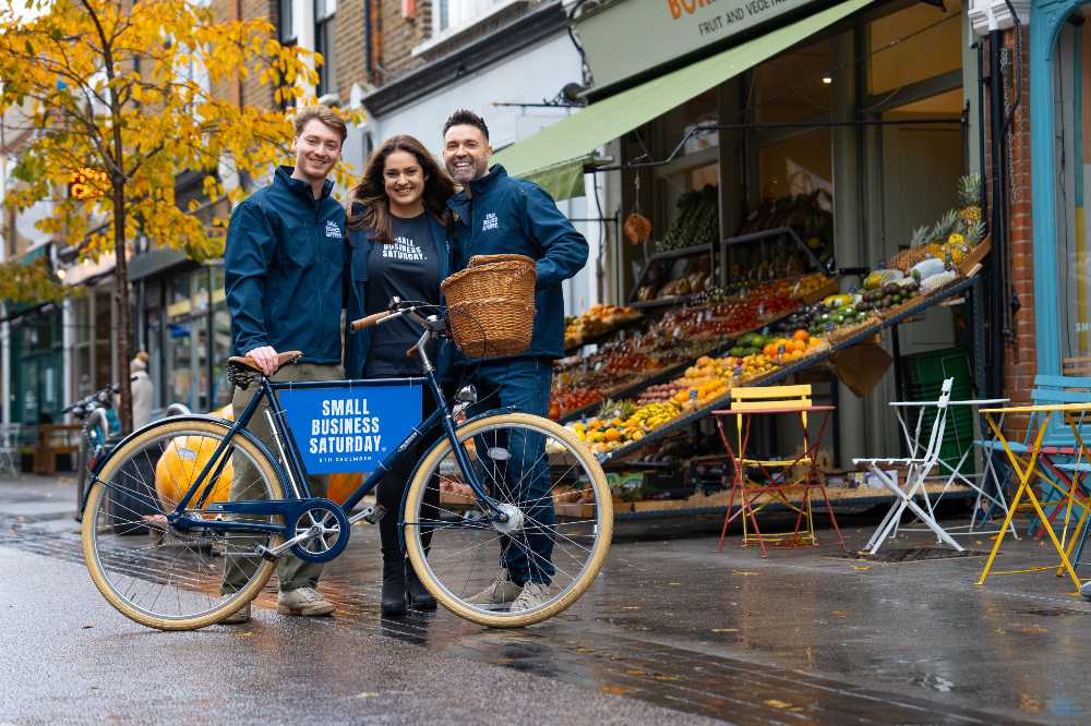 Three people stood on a high street outside a fruit and veg shop holding a bike with Small Business Saturday on it