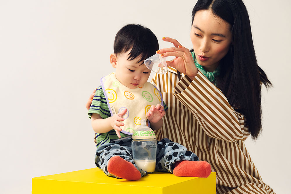 A mother stood next to a child sat down wearing a Tommee Tippee bid