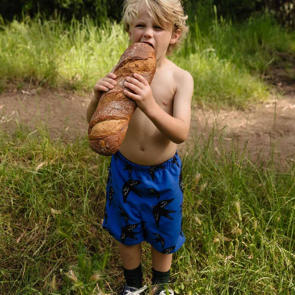 A child outside eating a baguette wearing blue swim shorts from YAY's Farnel collection 