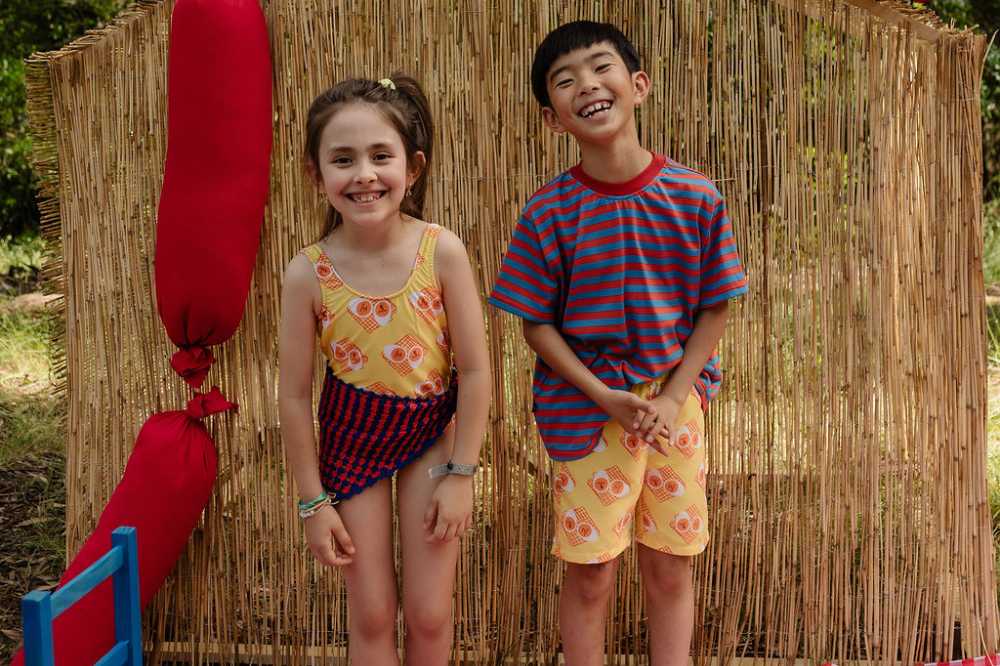 Two children stood in front of a grass hut wearing swimwear from YAY's Farnel collection