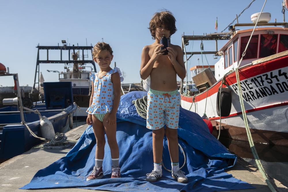 A boy and girl stood on a pier next to boats wearing Paper Boat's swimwear