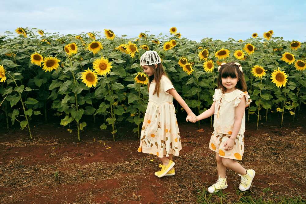 Two girls walking hand in hand in a sunflower field wearing sunflower print dresses