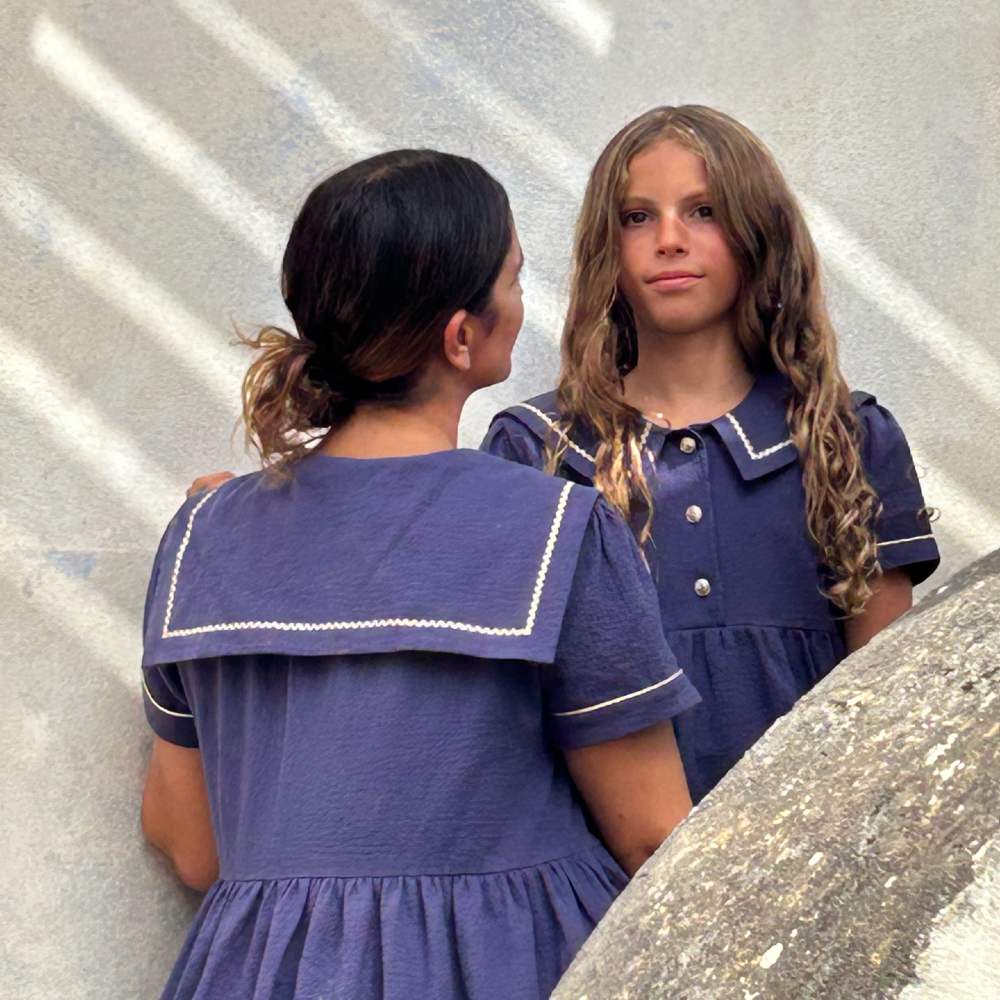 A woman a girl stood outside in blue sailor-style dresses