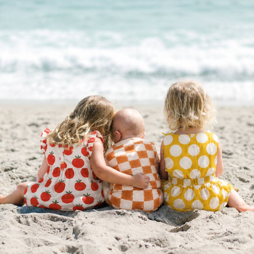 Three children sat together on a beach with their backs to the camera 