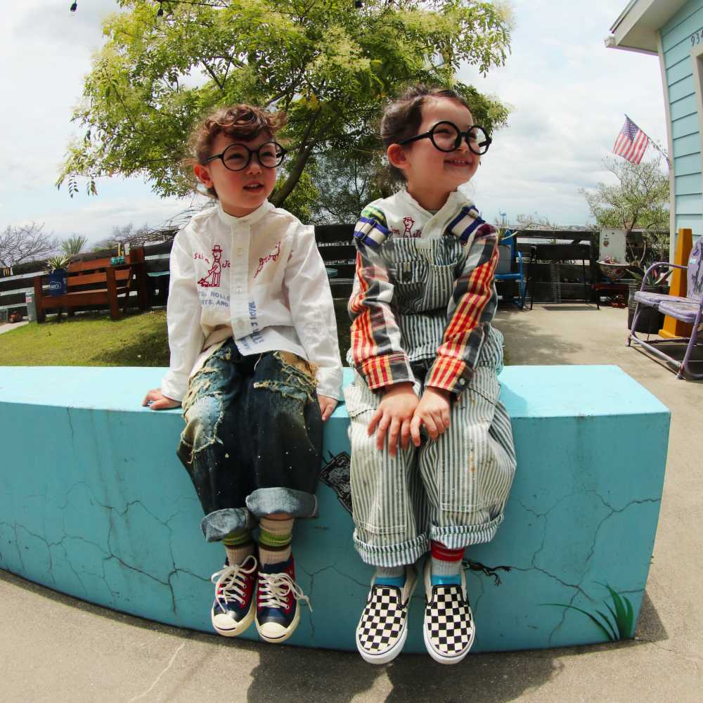 Two children in glasses sat outside on a blue wall