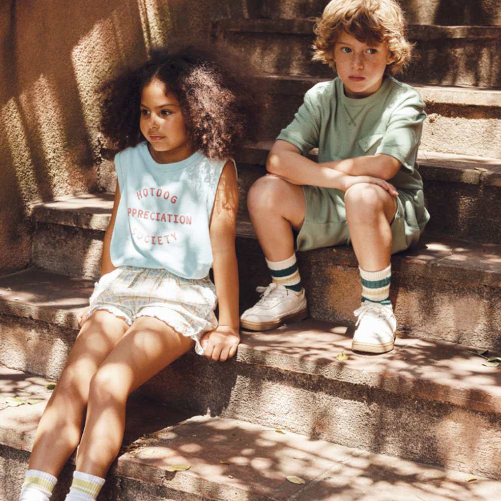Two children in shorts and T-shirts sat outside on some steps 