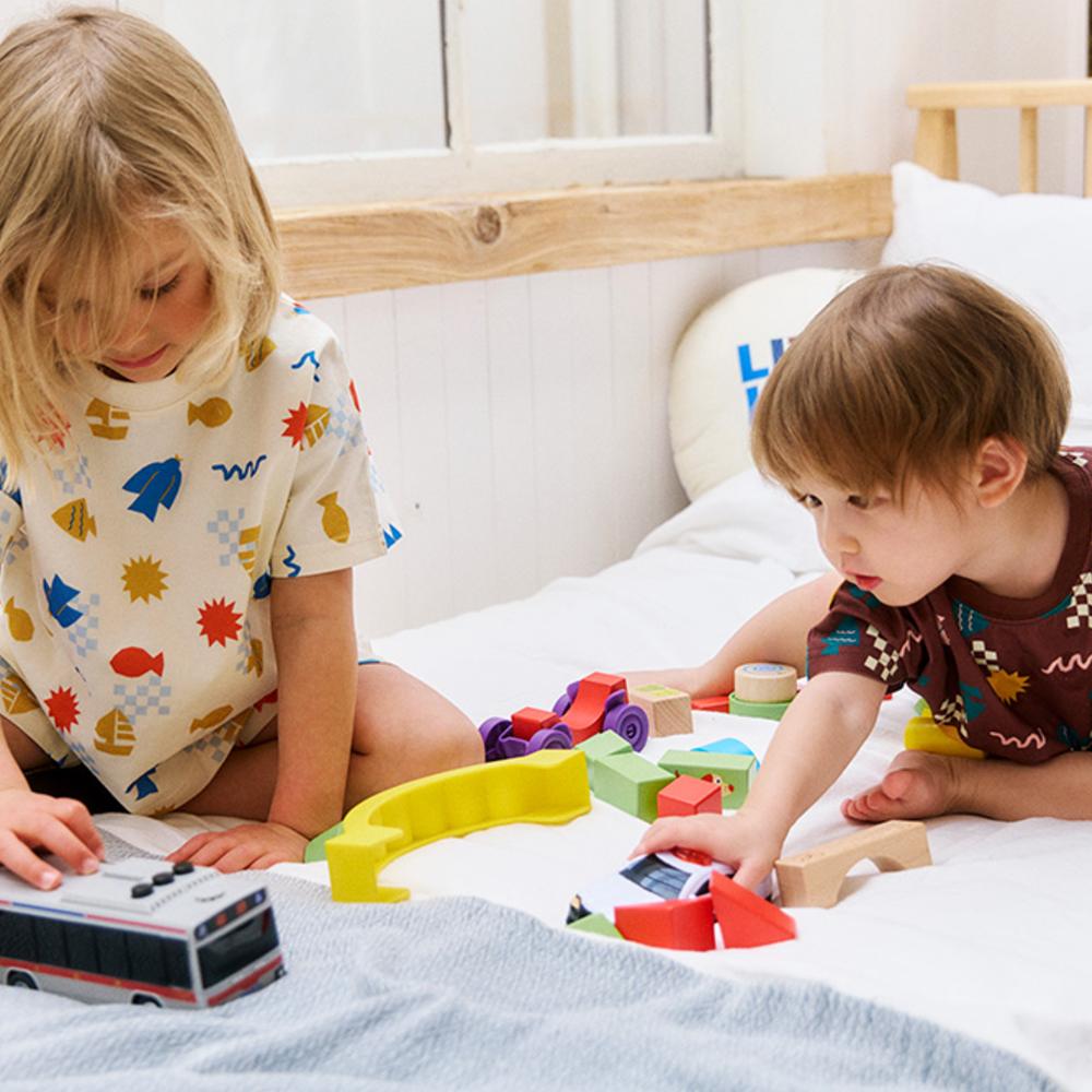 Two children wearing bold printed outfits playing with toys on a bed 