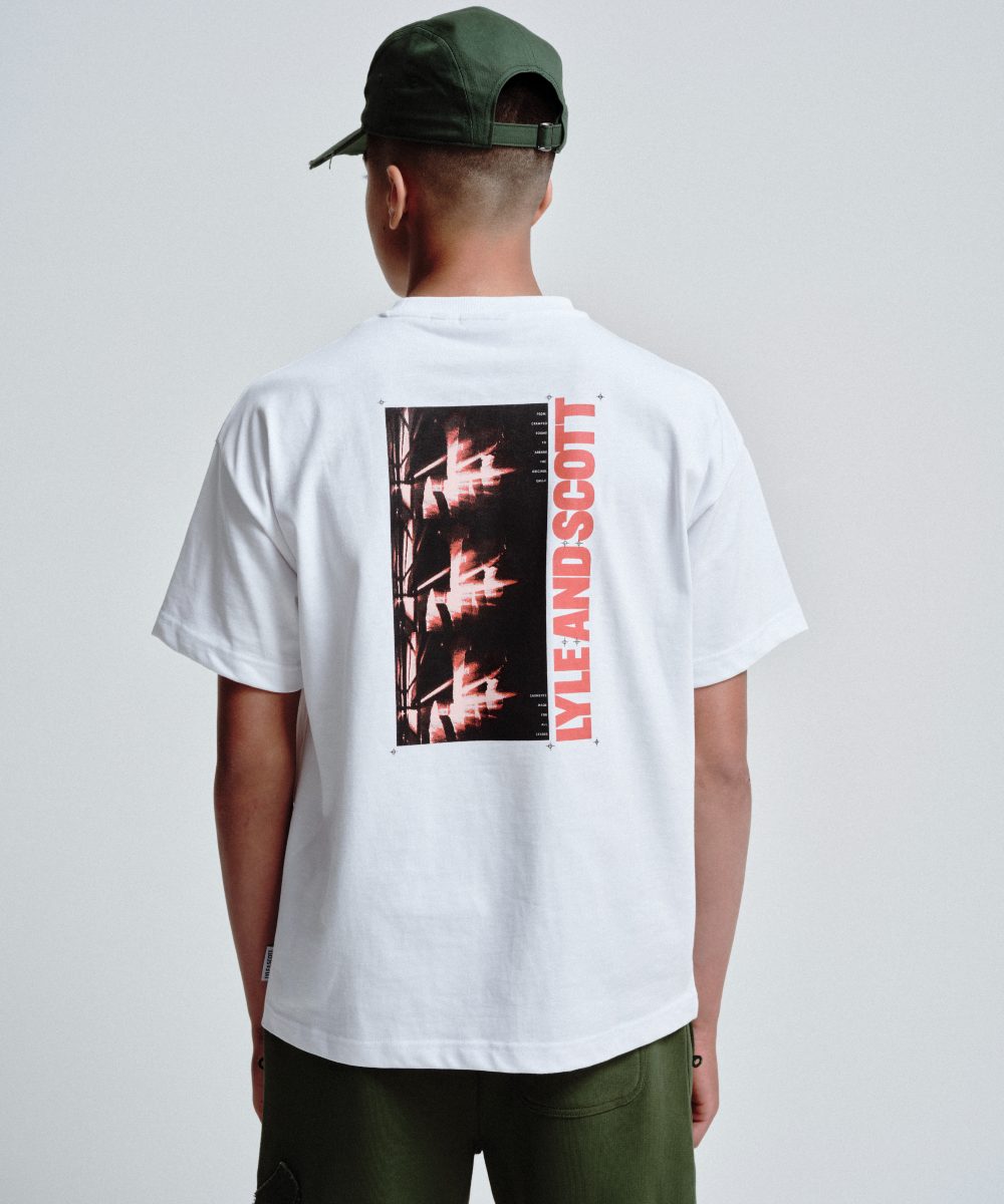 A boy with his back to the camera wearing a cap, graphic T-shirt and trousers by Lyle & Scott Kidswear