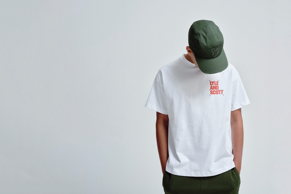A boy with his head down against a white background wearing a cap, T-shirt and trousers by Lyle & Scott Kidswear