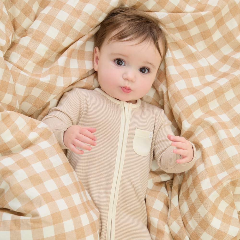 A baby in a babygro by MORI lying on a check print cover 