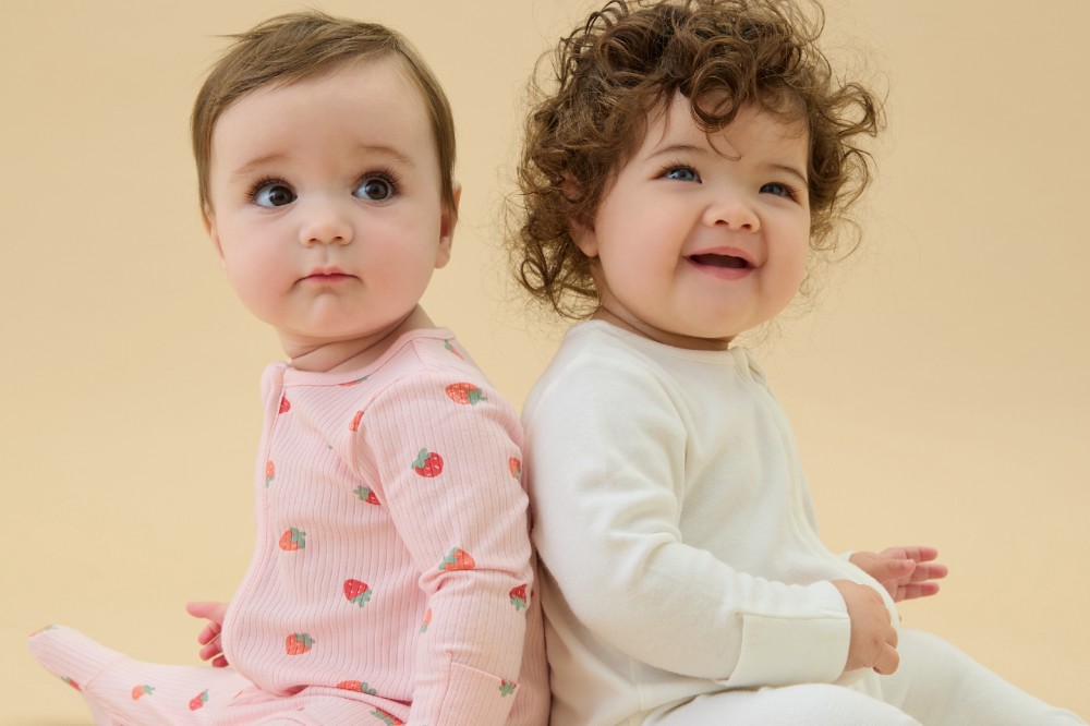 Two babies sat back to back wearing babygros by MORI