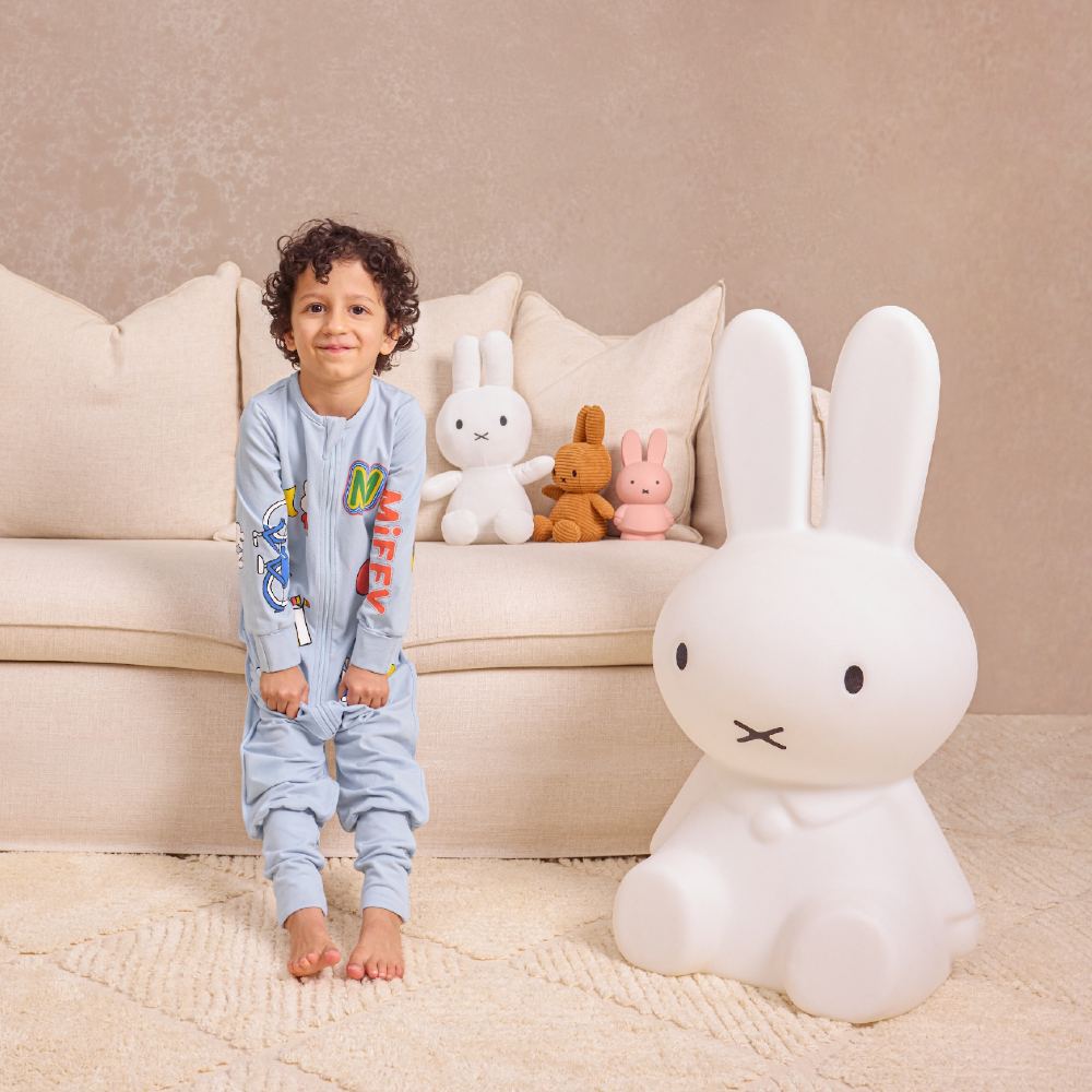 A boy wearing blue Miff pyjamas sat on a sofa beside Miffy toys