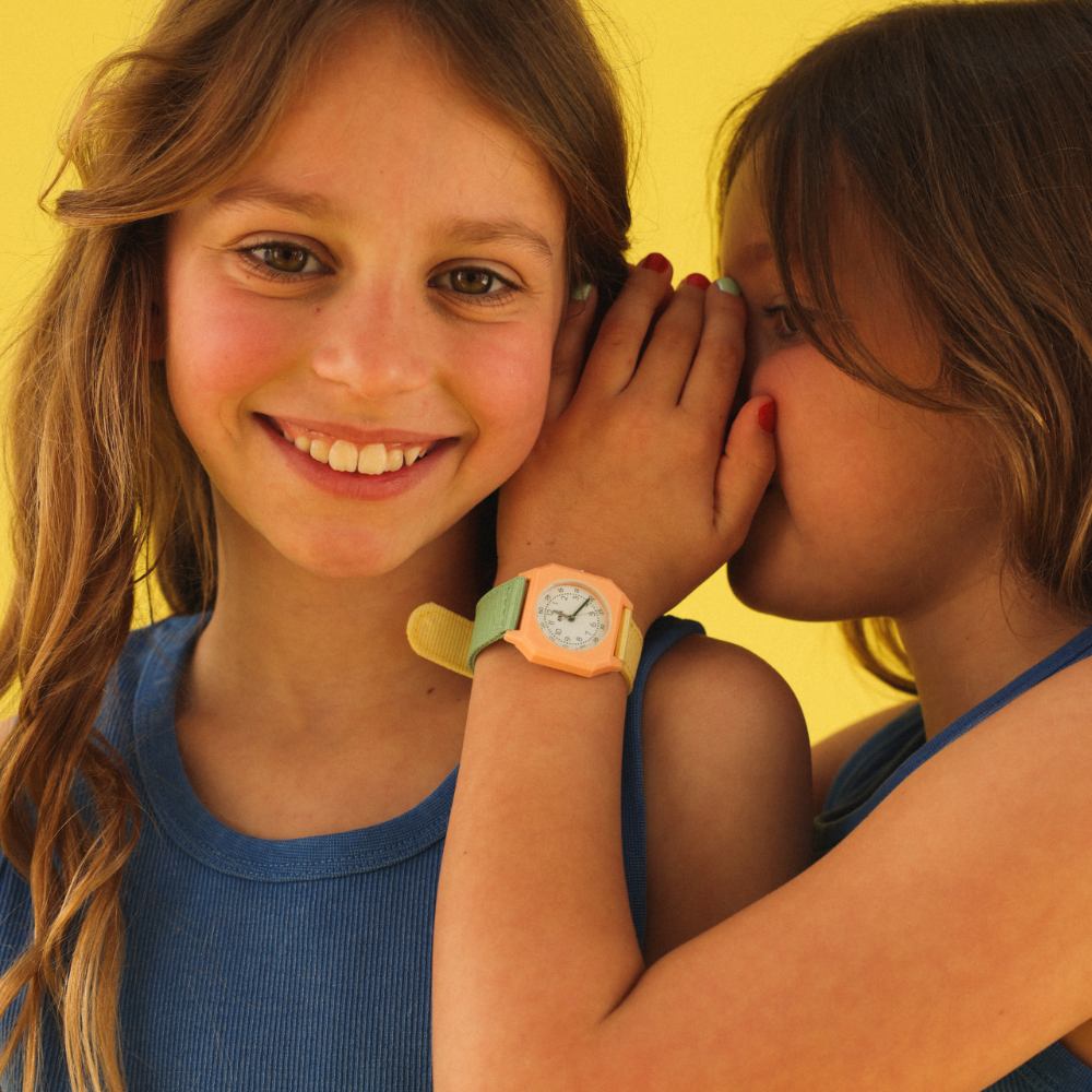A girl whispering in another girl's ear wearing a watch on her wrist