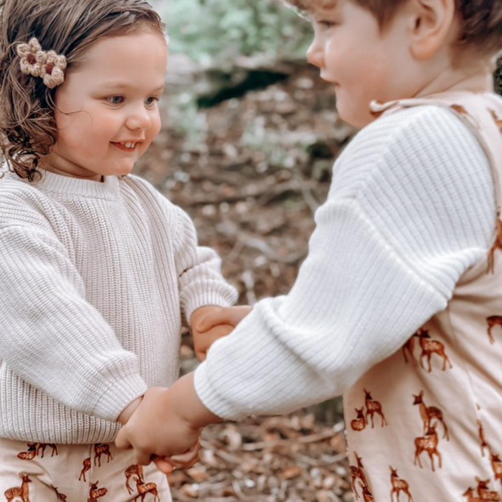 Two children outside holding hands wearing deer print outfits by Moon & Bear 