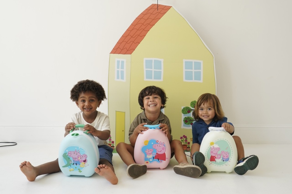 Three children sat in front of a play house with Peppa Pig My Carry Pottys