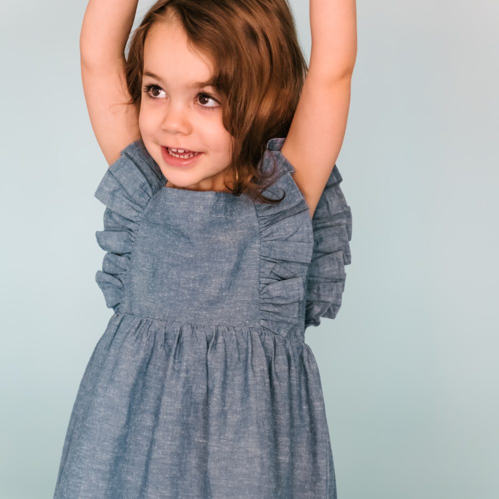 A girl wearing a blue frill dress holding her arms in the air 