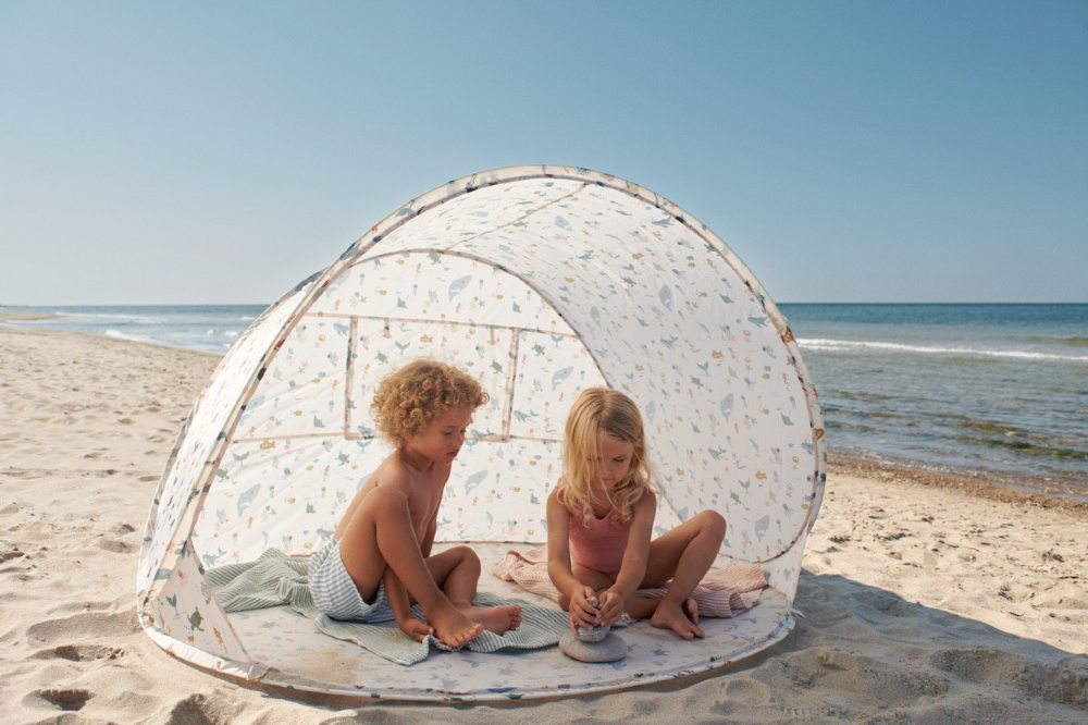 Two children sat under a UV tent on a beach