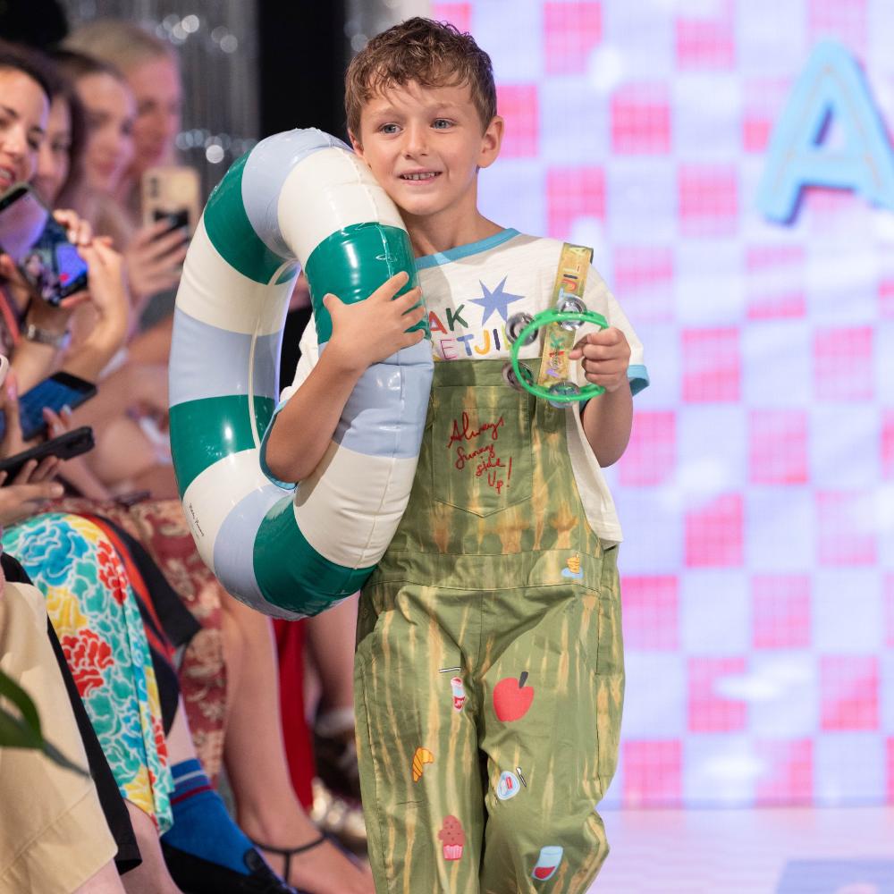 A boy holding a rubber ring walking down a catwalk at Pitti Bimbo