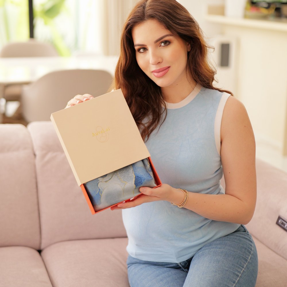 A woman holding a AuraLai Multi-Functional Nursing Cover in a gift box