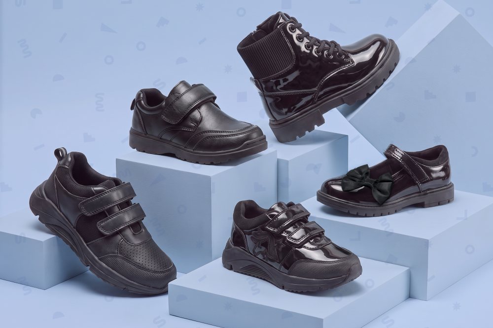 Five black Little Classmates school shoes displayed on a blue background