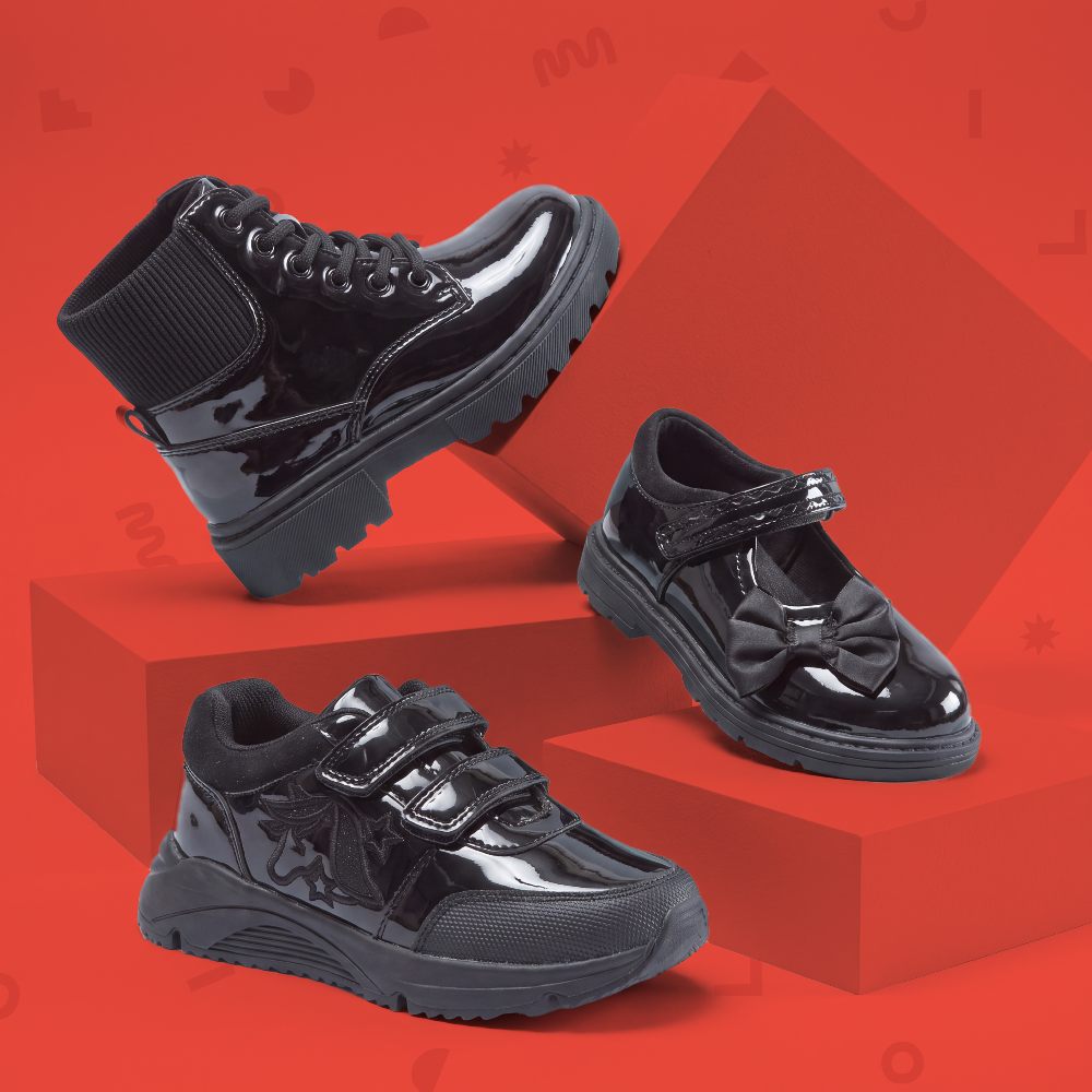 Three black Little Classmates school shoes shown against a red background 