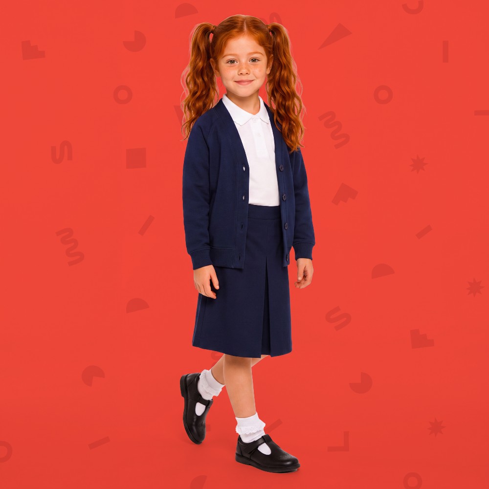A girl in Little Classmates school uniform stood against a red background 