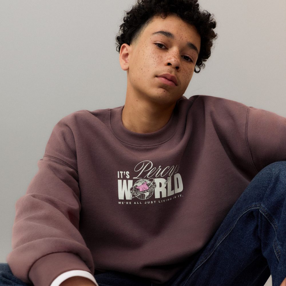 A boy sat on the floor wearing a brown sweatshirt from the M&S Percy Pig collection 