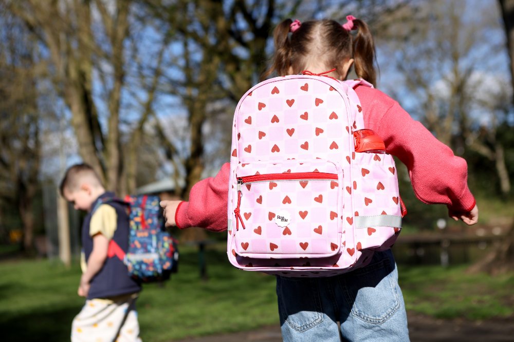 The back of two children outside wearing backpacks by Roamie