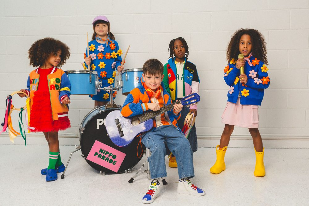 A group of children around a drum kit wearing brightly coloured clothing