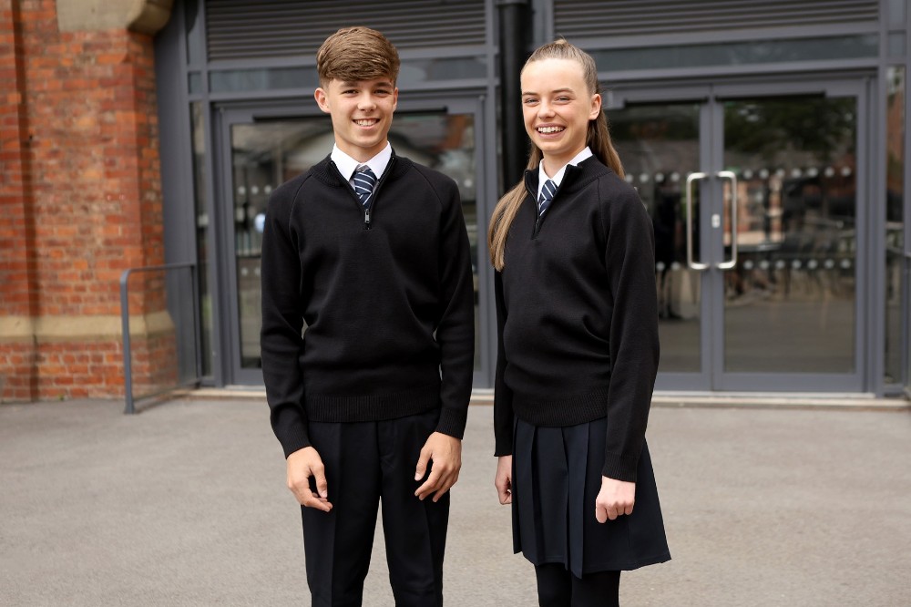 Two school pupils stood outside a school building wearing black school uniforms by Banner