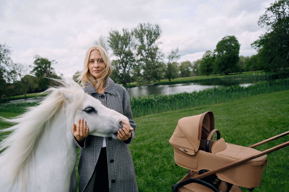A woman stood outside by a lake next to w white horse and a Bugaboo x Stella McCartney stroller