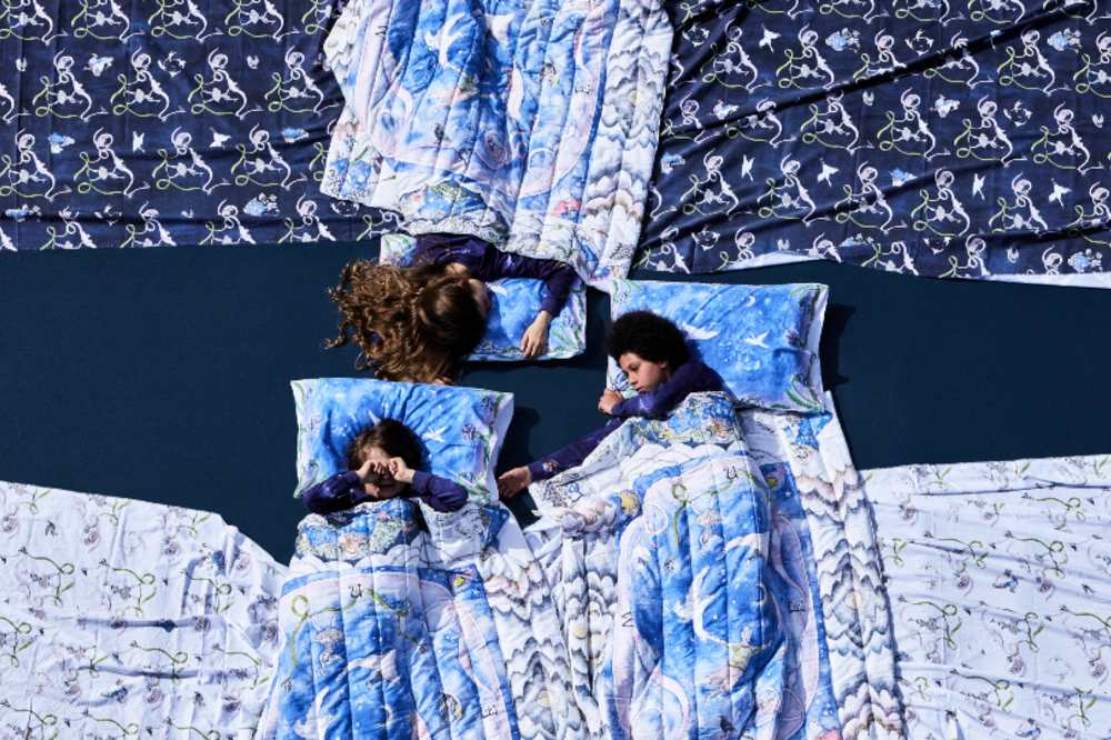 Three children laid together on the floor in illustrated sleeping bags