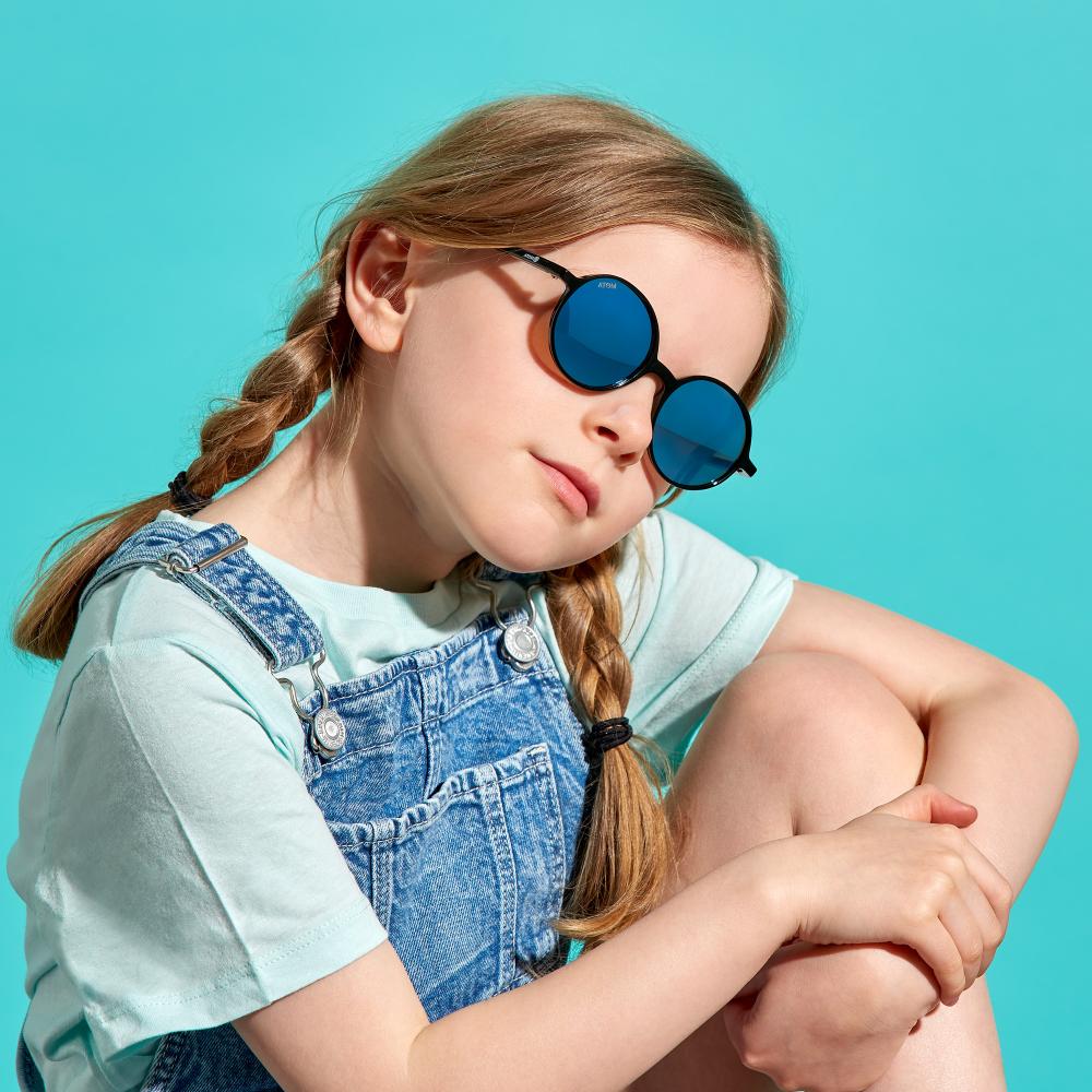 A child sat against a blue background wearing sunglasses 