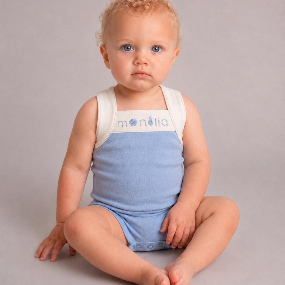 A baby sat on the floor wearing a pale blue and white playsuit 