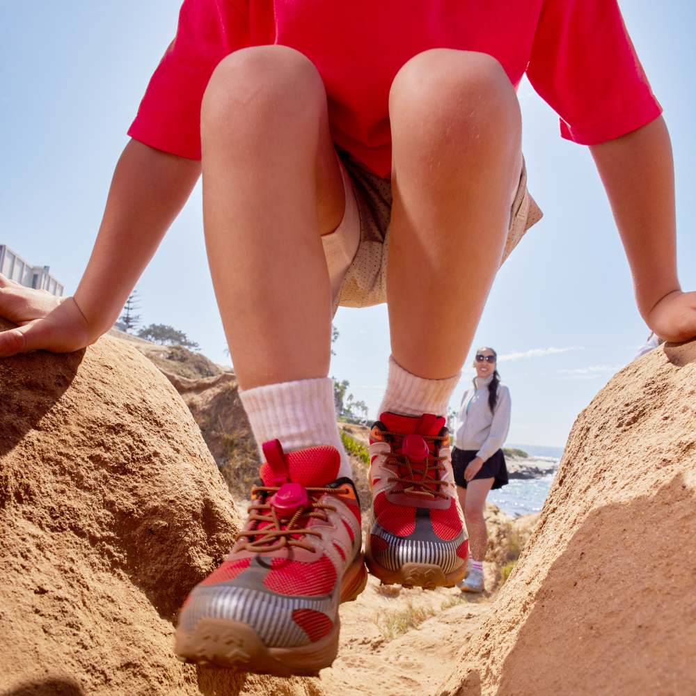 A child climbing on a rock wearing a red top and shoes 