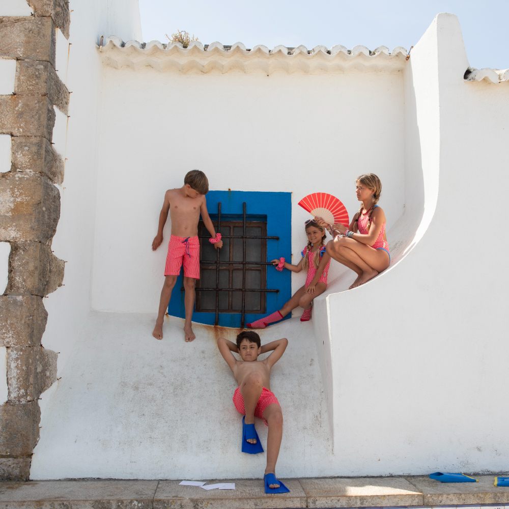 Children in matching swimwear outside a white building 