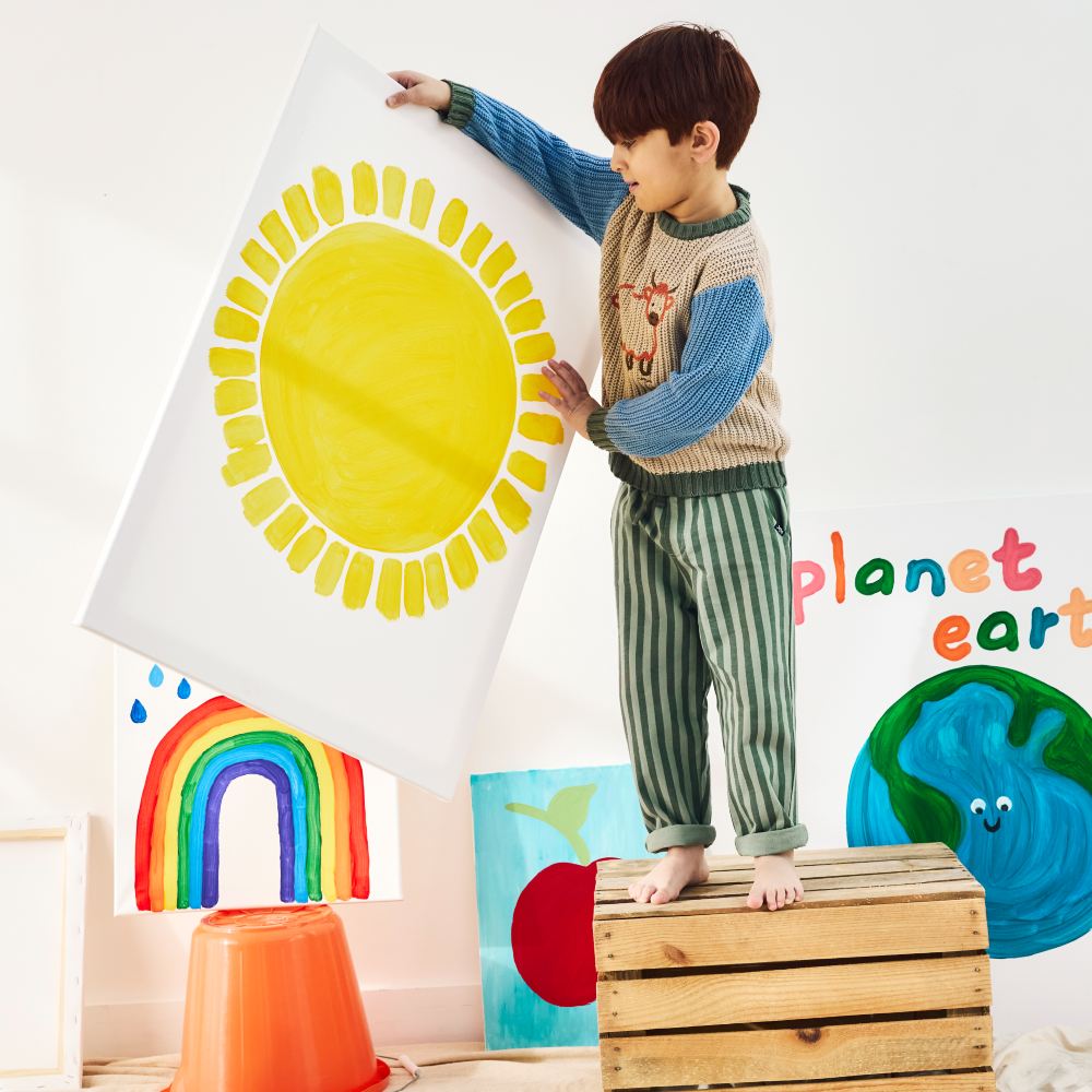 A boy stood on a wooden crate holding a painting of the sun