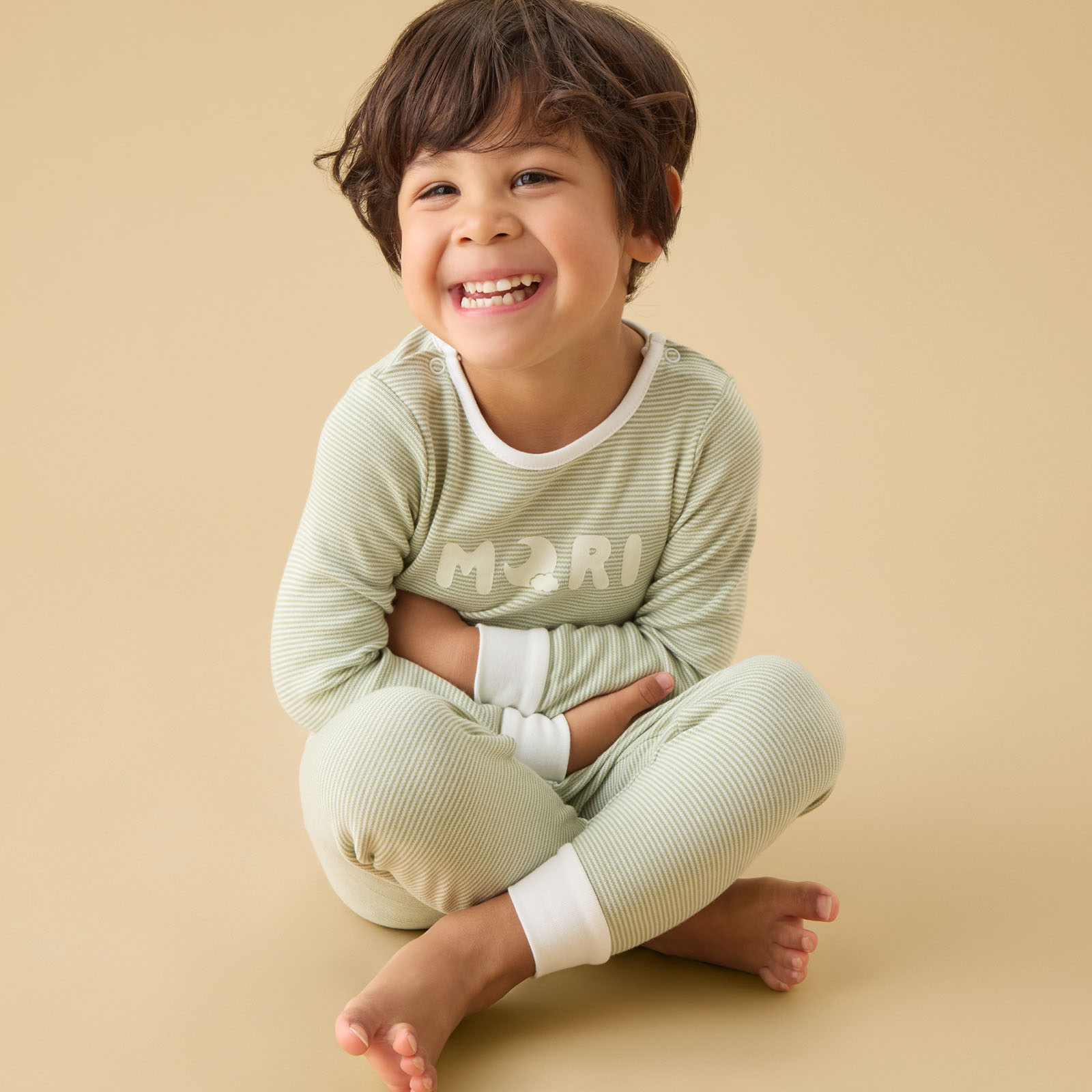 A laughing child sat on the floor wearing MORI pyjamas 